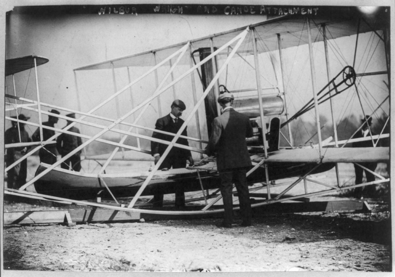 Wilbur_Wright_examining_canoe_attachment_to_aeroplane_before_1st_flight_over_water_(3b25549u)[1]